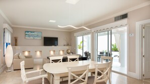A modern living room with a dining area, a flat-screen TV, and a large window. - Vacation Home "Villa 82" with Mountain View, Pool & Wi-Fi (Corralejo)