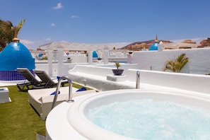 Uma área de piscina no terraço com espreguiçadeiras, uma banheira de hidromassagem e vista para prédios ao fundo.