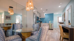 A modern kitchen with a round glass table and blue patterned chairs, a stainless steel refrigerator, and a blue-tiled backsplash. - Ahoy Mate! with Compass Realty at the Truman Annex in Key West (Key West)