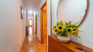 Un couloir avec une commode en bois, un miroir et un vase rempli de tournesols.