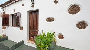 A white building with a wooden door, a window with shutters, and a potted plant with flowers. - Vacation Home 'Casa Haba' with Sea View, Terrace & Wi-Fi (Sauzal)