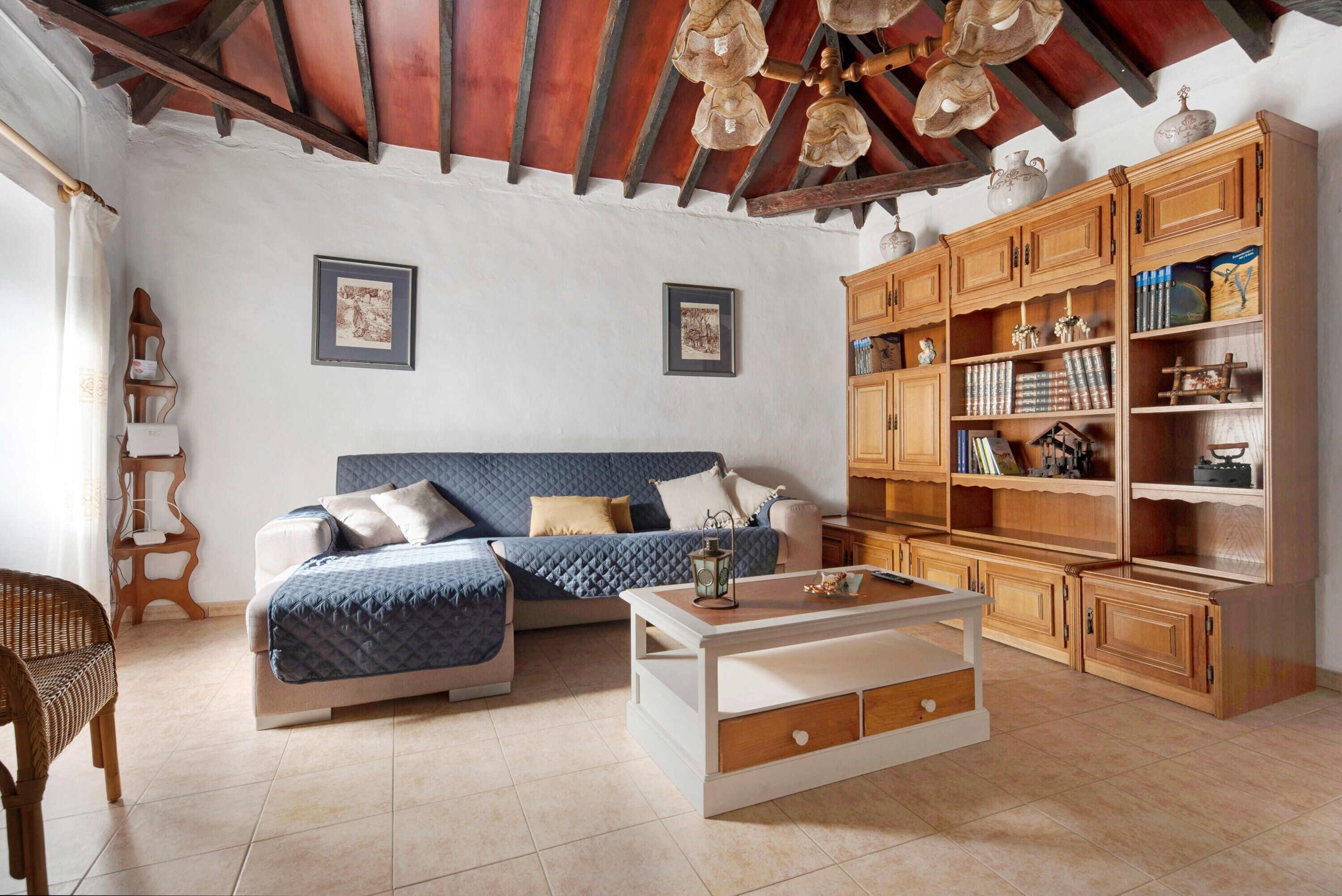 Una habitación con cama, sofá, una mesita de centro, armarios de madera y un techo con vigas a la vista.