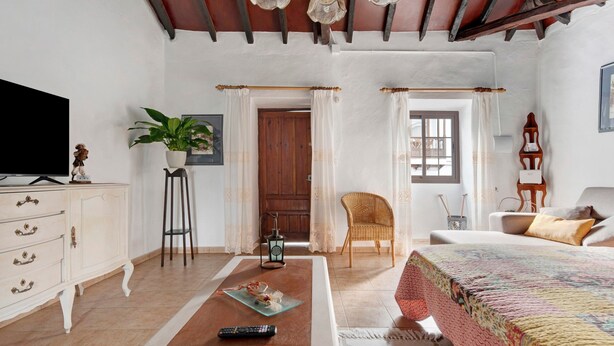 A bedroom with a bed, a TV, a coffee table, a chair, a plant, and a door leading to another room. - Vacation Home 'Casa Haba' with Sea View, Terrace & Wi-Fi (Sauzal)