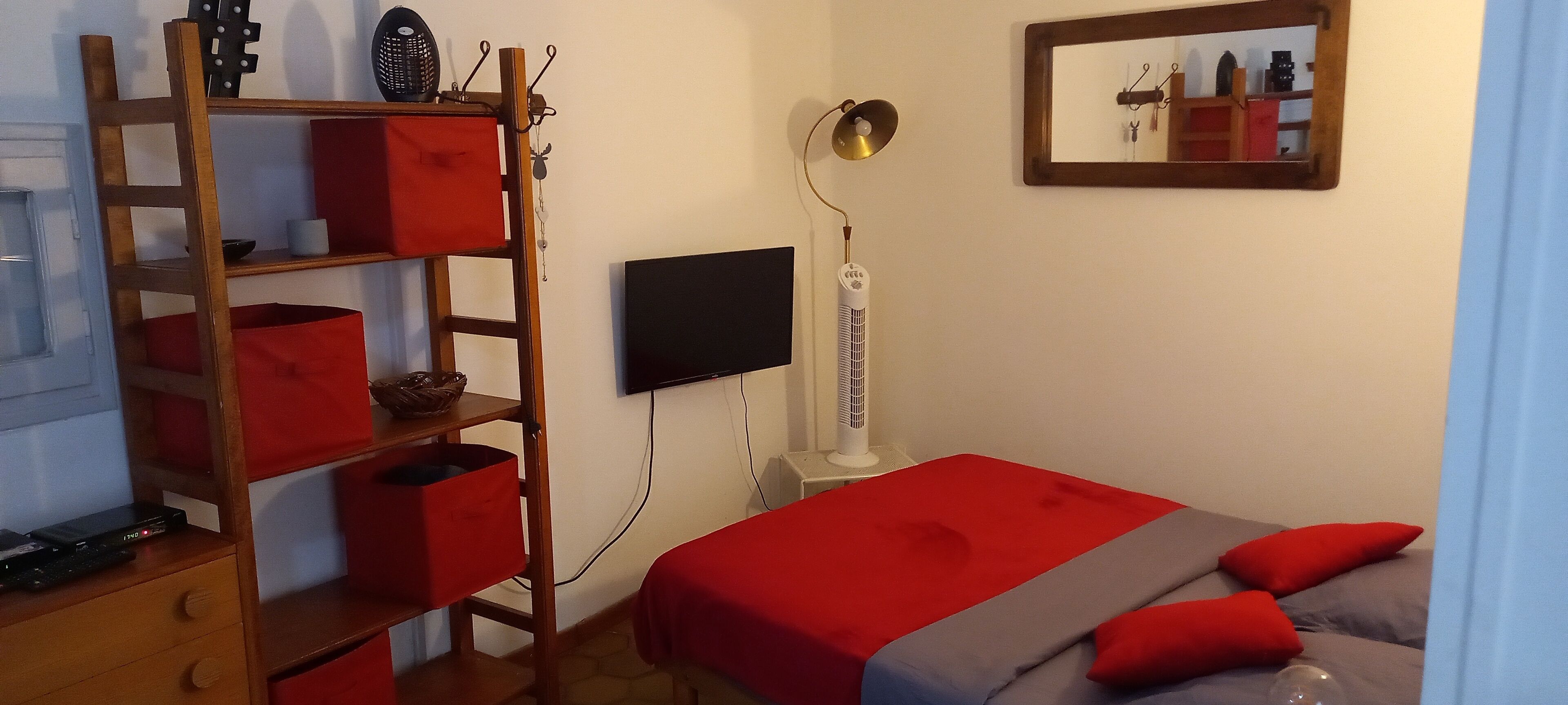 Un dormitorio con cama, televisor, calefactor y estante de madera con cajas rojas.