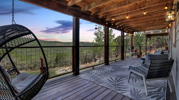 A wooden deck with a hanging chair, a cushioned bench, and a view of the landscape. - Painted Paradise Guest Suite | Romantic Hill Country Sunsets with a swimming poo (New Braunfels)