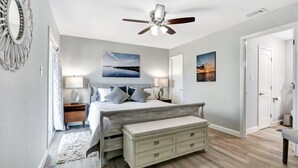A bedroom with a bed, bedside tables, a bench, a ceiling fan, and artwork on the walls. - Painted Paradise Guest Suite | Romantic Hill Country Sunsets with a swimming poo (New Braunfels)