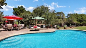 A swimming pool with a wooden deck, lounge chairs, and a gazebo. - Painted Paradise Guest Suite | Romantic Hill Country Sunsets with a swimming poo (New Braunfels)