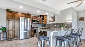 A modern kitchen with wooden cabinets, stainless steel appliances, a granite countertop, and bar stools. - Painted Paradise Guest Suite | Romantic Hill Country Sunsets with a swimming poo (New Braunfels)