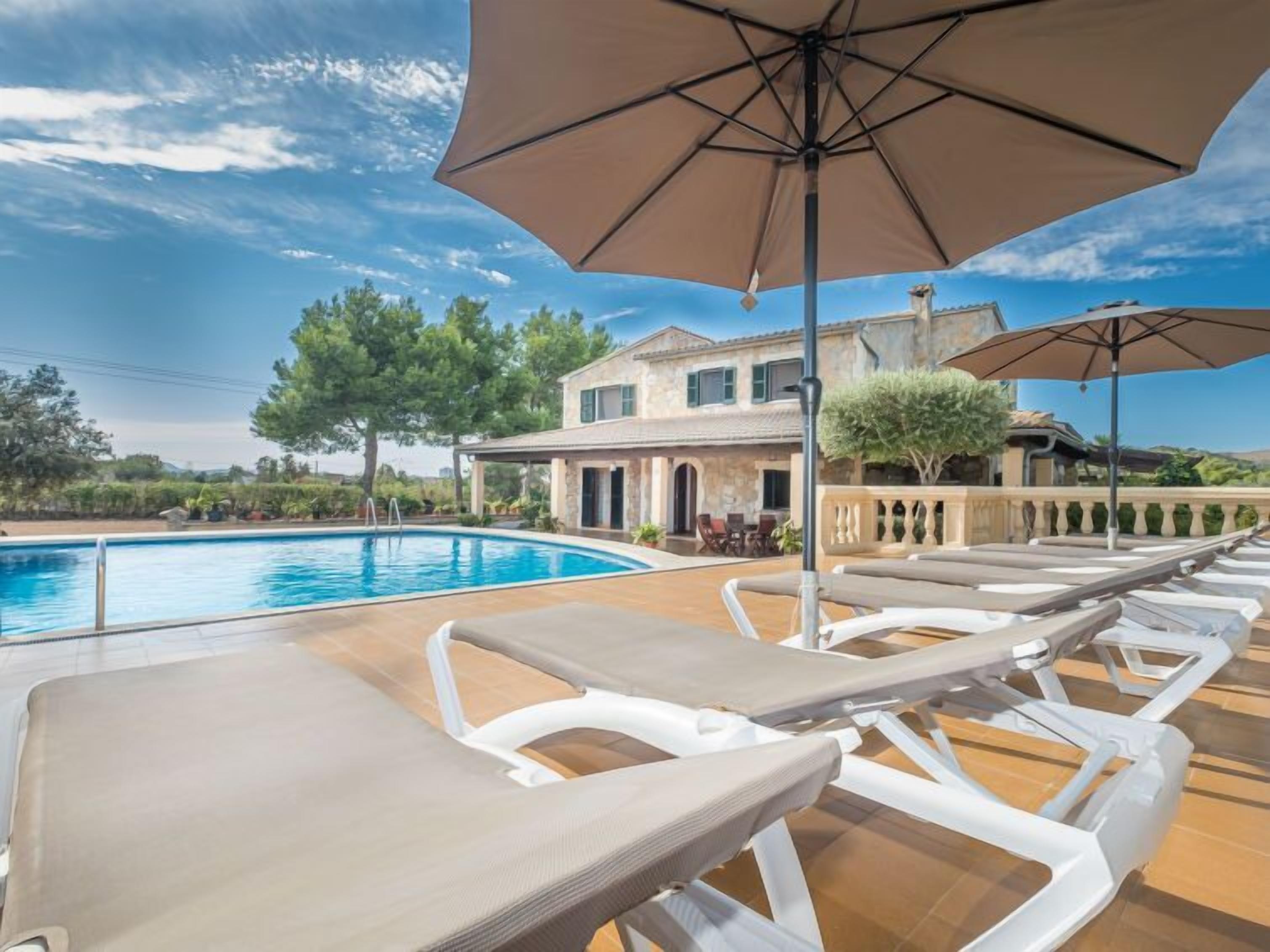 A poolside area with lounge chairs and umbrellas, a pool, and a building with a stone facade in the background.