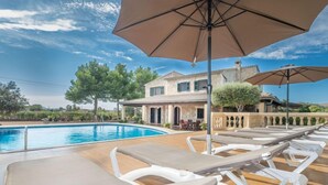 A poolside area with lounge chairs and umbrellas, a pool, and a building with a stone facade in the background. - Can Cerda by Interhome (Alcúdia)