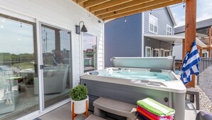 Un jacuzzi en un patio cubierto con puerta de vidrio, una planta pequeña y una pila de toallas.