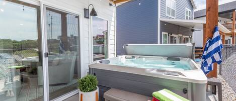 A hot tub on a covered patio with a glass door, a small plant, and a stack of towels.