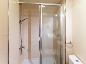 Een douchecabine met glazen wanden, een handdouche en een wandmengkraan.