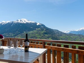 A table with wine glasses and a bottle on a wooden deck with a mountain view. - Les Crêtes 1 by Interhome (Veysonnaz)