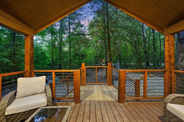 Une terrasse en bois, meublée de meubles en osier, avec vue sur une forêt.