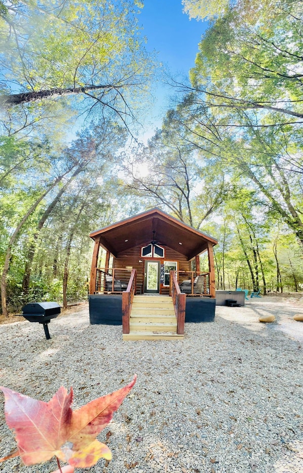 A wooden cabin with a porch, steps leading to the entrance, and a grill outside.