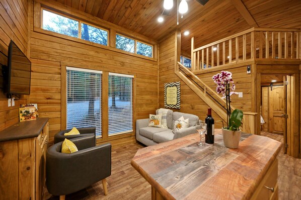 A wooden cabin interior with a sofa, dining table, and staircase.