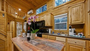 Une cuisine en bois dotée d’un îlot central, d’un four à micro-ondes encastré et d’une fenêtre avec des stores.