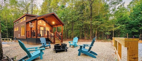 Una cabaña con terraza, asientos al aire libre y un hogar para fogata.