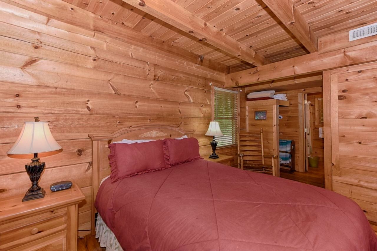 Un dormitorio de cabaña de madera con una cama, dos mesitas de noche y una mesilla.