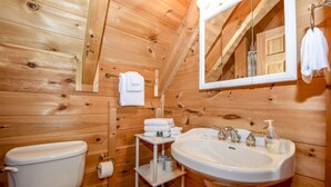 A wooden cabin bathroom with a toilet, sink, and mirror. - Whisper Creek 2 Bedroom Cabin by RedAwning (Townsend)