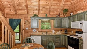 A wooden cabin kitchen with a dining table, chairs, a refrigerator, stove, and cabinets. - Whisper Creek 2 Bedroom Cabin by RedAwning (Townsend)