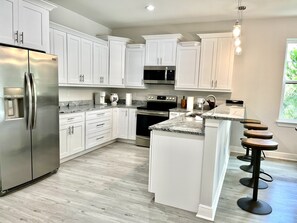 Uma cozinha moderna com armários brancos, eletrodomésticos de aço inoxidável, bancada de granito e um espaço com banquetas.