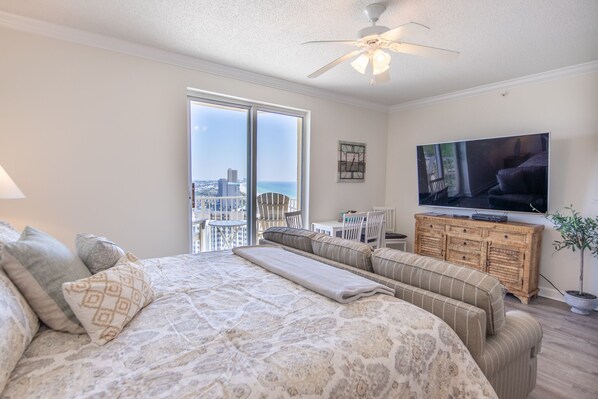 Ein Schlafzimmer mit einem großen Bett, einem Fernseher, einem Deckenventilator und Blick auf die Stadt durch große Fenster.