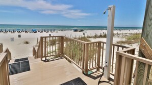 A wooden deck with a metal handrail, leading to a sandy beach with umbrellas and beach chairs.