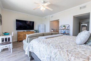 Ein Schlafzimmer mit Bett, Fernseher, Kühlschrank, einem Holzk dresser und einer Pflanze.