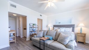 A living room with a sofa, two side tables, a ceiling fan, and a door leading to another room.