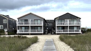 Ein Anwesen am Strand mit einer Holzstege, der zu einem zweistöckigen Gebäude mit Balkonen führt.
