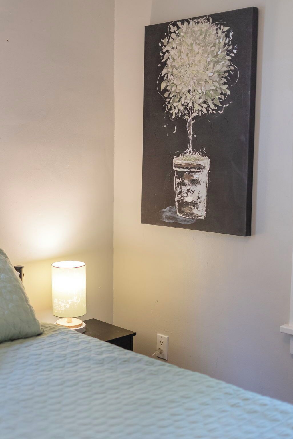 Een slaapkamer met een bed, een bedlampje en een schilderij van een bloem in een vaas.