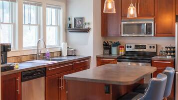 A modern kitchen with wooden cabinets, stainless steel appliances, a built-in island with bar stools, and pendant lighting.