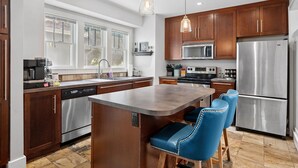 A modern kitchen with wooden cabinets, stainless steel appliances, a central island with bar stools, and pendant lighting.