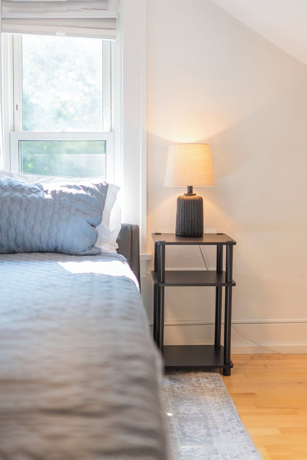 Una camera da letto con un letto, una finestra, un comodino con una lampada e un tappeto decorato.