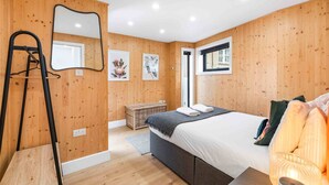Ein Schlafzimmer mit Holzwänden, einem Bett, einem Spiegel, einem Fenster und einer Tür.