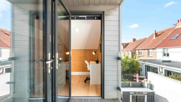 Eine moderne Wohnung mit Glastür zu einem Holzinnenraum, einem kleinen Balkon und Blick auf Nachbarhäuser.
