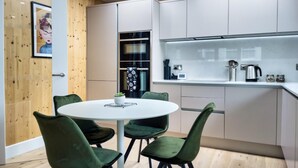 Une cuisine moderne avec des armoires blanches, une table de salle à manger ronde entourée de chaises vertes et un mur d’accent en bois.