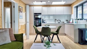 Une cuisine moderne avec des meubles blancs, un coin repas doté d’une table en verre et de chaises vertes, et un canapé vert agrémenté d’une plante posée sur la table.