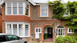 Une maison à deux étages avec une baie vitrée, une porte d’entrée en arc de cercle et une voiture garée devant.