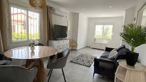 A modern living room with a dining area, a sofa set, a television, and a large window.