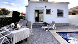 A white villa with a stone patio, a pool, and outdoor seating.