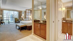 Ein Hotelzimmer mit einem großen Bett, einem Schreibtisch, einem Sessel, einer Sitzecke und einem Esstisch, mit Blick auf die Stadt.