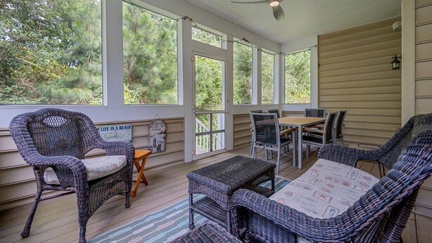 Eine überdachte Veranda mit Korbmöbeln, einem Deckenventilator und Blick auf Bäume.