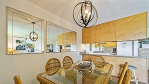 A dining area with a glass table, wicker chairs, and a chandelier. - Maui Sunset Vacation Rentals A319 (Kihei)