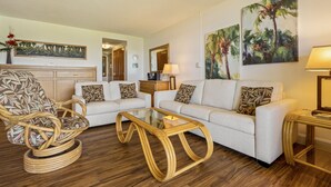 A living room with a wicker chair, a sofa, a glass coffee table, and two paintings on the wall. - Maui Sunset Vacation Rentals A319 (Kihei)