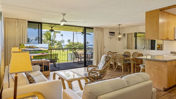 A spacious living area with a balcony, wicker furniture, and a view of the outdoors. - Maui Sunset Vacation Rentals A319 (Kihei)