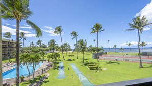 A pool area with palm trees, a tennis court, and a view of the ocean. - Maui Sunset Vacation Rentals A319 (Kihei)