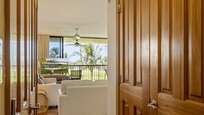 A room with a wooden door, a white sofa, and a view of a balcony with outdoor furniture. - Maui Sunset Vacation Rentals A319 (Kihei)